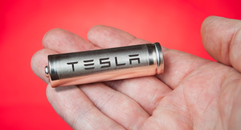 Hand holding a Tesla battery cell on red bacxkground