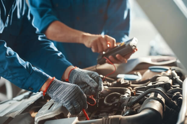 Two auto mechanics looking for an electrical problem using a multimeter