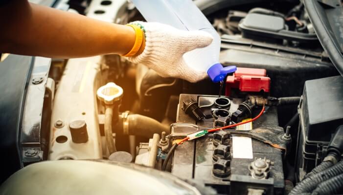 Auto mechanic refilling the water level in a car battery