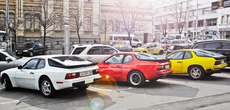A white, a red and a yellow Pörsche 944 parked in a parking spot