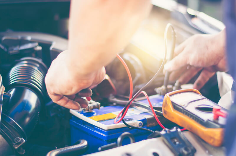 Auto mechanic testing a car battery using a multimeter