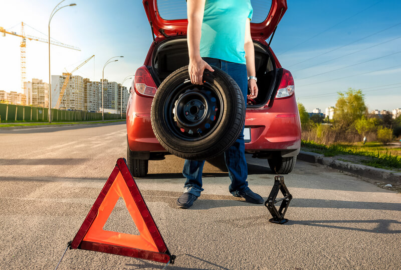 Man using reflective triangle to safely change a car tire