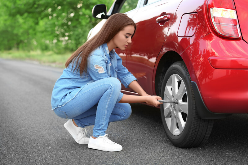 Woman uses a wrench to remove a car tire