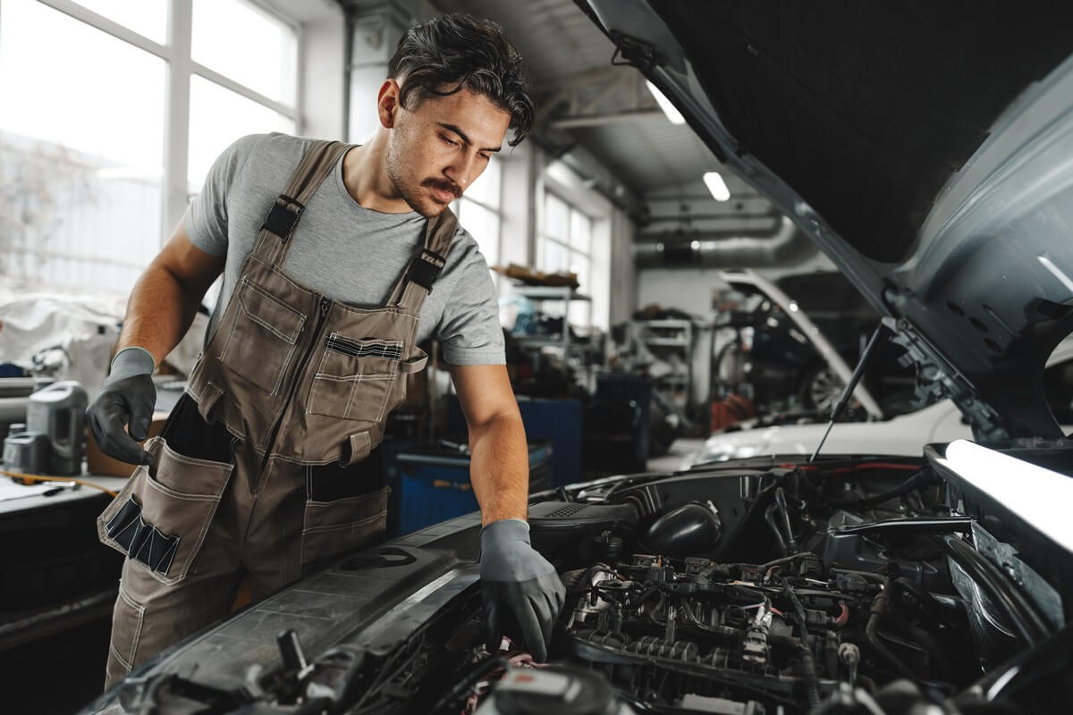 Young male mechanic performing inspection on a car engine